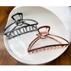 Elegant geometric metal hair claws in black and rose gold on a minimalist white bowl