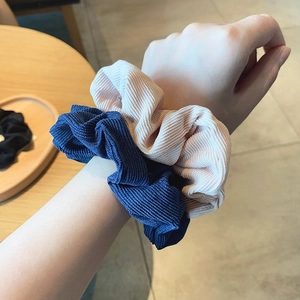 Pink and navy corduroy scrunchies worn on wrist over a natural wooden table