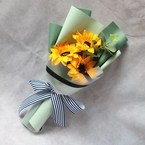 Macro shot of artificial sunflower bouquet with green paper wrap and striped ribbon
