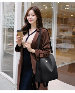 Chic black nylon backpack with gold hardware worn over one shoulder in an urban setting