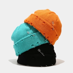 Zerstörte Strickmütze mit Eisenringen und Nadeln in Orange, Blau und Schwarz