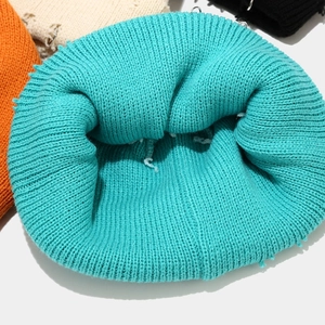 Detail der petrolblauen Strickmütze mit Löchern und Metallring-Accessoires