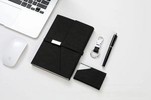 Close-up of black leather notebook, metal keychain, and pen set in a modern office desk scene