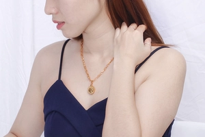 Golden coin pendant necklace with queen portrait shown on a neck of a model