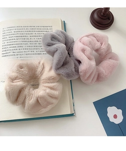 Close-up of plush hair scrunchies in beige, gray, and pink on an open book