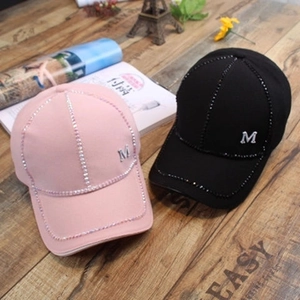 Black and pink baseball caps with rhinestone stripes and metal M logo on wooden table