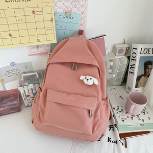 Dettaglio di uno zaino rosa minimalista con un ciondolo a forma di cucciolo e tasca laterale