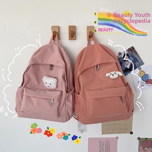 Dettaglio di zaini in nylon rosa con accessori di peluche su ganci in legno