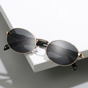 Lunettes de soleil ovales monture dorée et verres foncés sur un support minimaliste
