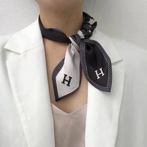 Détail d'un foulard en soie sergé monochrome avec motif lettre H noué sur le mannequin
