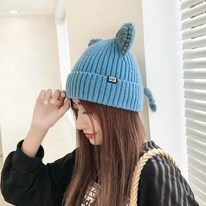 Blue knitted beanie with cute cat ears and CAT logo tag worn by a model in bright light