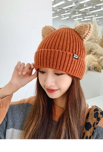 Close-up of orange knit beanie with cat ears and a black CAT label detail