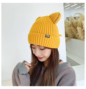 Detailed close-up of yellow knit beanie with cat ears and small CAT woven label