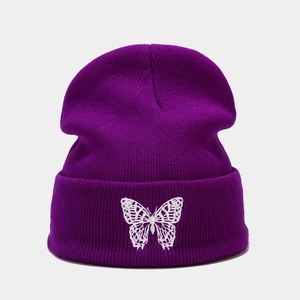 Close-up of intricate white butterfly embroidery on a dark purple knitted beanie hat