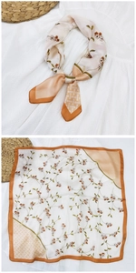 Dettaglio di un foulard quadrato in seta con motivo floreale crema, arancione e verde