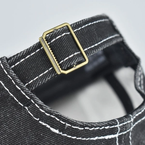 Detailansicht der bronzenen Metallschnalle und Kontrastnähte auf der gewaschenen Denim-Kappe