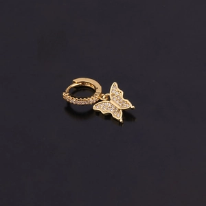 Détail d'une boucle d'oreille papillon dorée avec zircons brillants sur fond noir