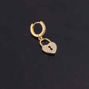 Vue macro de boucles d'oreilles cadenas cœur dorées avec zircons sur fond noir poli