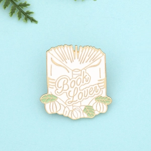 Detailed view of an open book enamel pin with Book Lover text and autumn pumpkin accents
