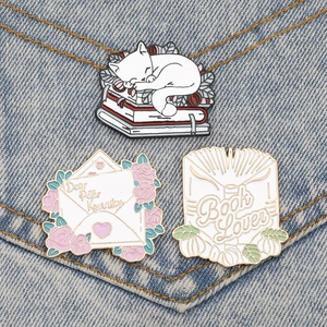 Detailed view of cat, letter, and book enamel pins set on blue denim fabric background