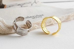 Detailed view of hammered irregular gold and silver open rings on a beige fabric