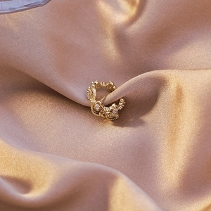 Macro shot of gold hollow crown ear cuff with white zircon stones on silk fabric