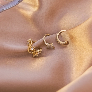 Macro shot of three gold ear cuffs with cubic zirconia star and moon designs on satin