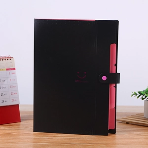 Trieur vertical noir avec onglets roses et motif sourire posé sur un bureau en bois