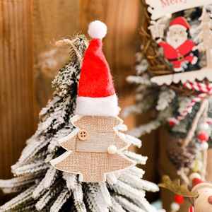 Handcrafted Christmas tree wooden ornament with red plush hat and burlap on snowy pine