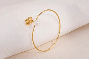 Detail of gold clover bangle featuring a single pearl on a beige fabric background