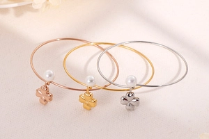 Close-up of three stackable pearl and clover charm bracelets in gold, silver, and rose gold