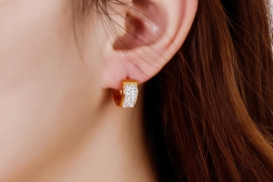 Close-up of small gold hoop earring with white pavé zircons on a female model