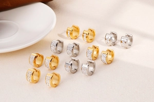 Close-up of gold and silver huggie earrings with cubic zirconia rows on textured linen