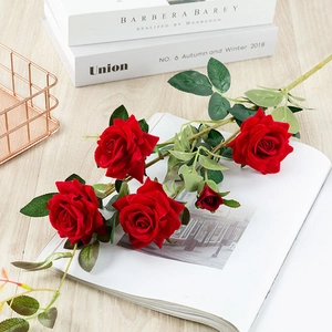 Close-up of red artificial silk roses with realistic green leaves on a light wooden table