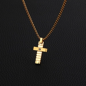 Close-up of golden cross pendant with black gem on textured box chain necklace