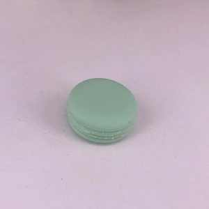Macro detail of a mint green macaron shaped plastic container on a soft pink surface