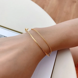 Detail of minimalist gold-plated bangle and delicate snake chain set on woman's wrist