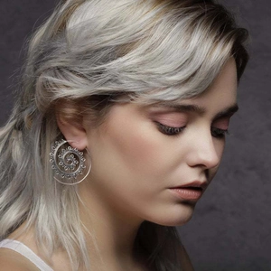 Macro detail of large silver spiral lotus earrings with intricate bohemian patterns