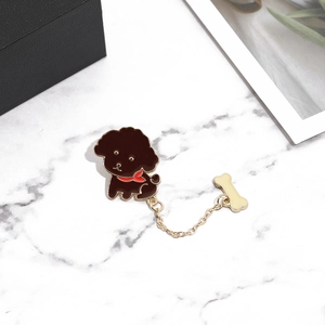 Detail of a golden poodle brooch with chain and bone pendant on marble surface