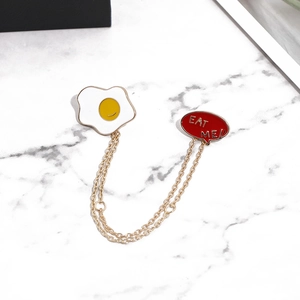 Détail de la broche émaillée œuf au plat et EAT ME avec double chaîne dorée élégante