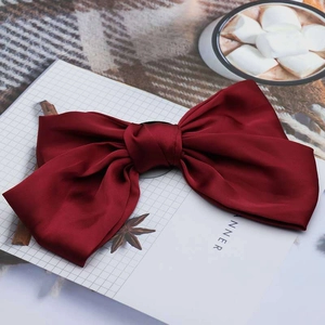 Macro detail of wine red oversized silk bow hair clip with polished satin texture