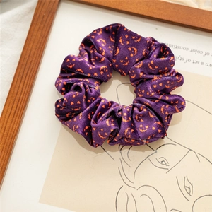 Close-up of velvet Halloween hair scrunchie with orange pumpkin print on purple fabric