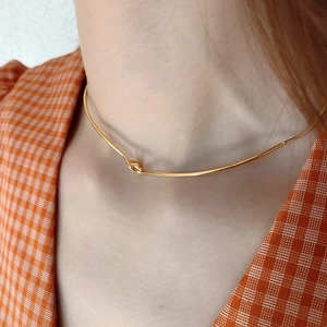 Close-up of minimalist gold knot necklace on model wearing orange plaid shirt