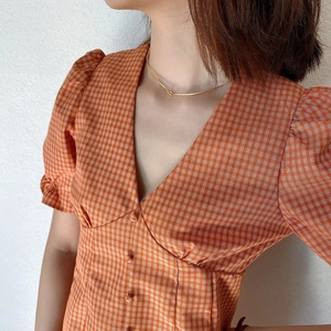 Detail of minimalist gold chain necklace on a model wearing an orange checkered V-neck top
