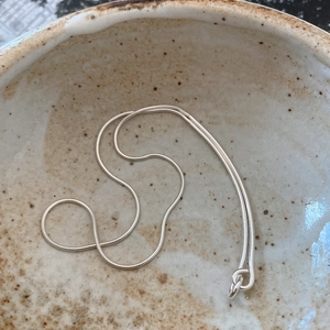 Macro shot of polished silver snake bone chain necklace inside a beige ceramic bowl