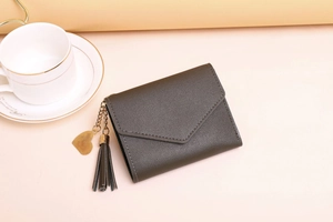 Detail of dark grey tri-fold wallet with lychee leather texture and heart tassel pendant