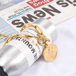 Minimalist gold pearl chain bracelet with embossed coin pendant on a lifestyle backdrop