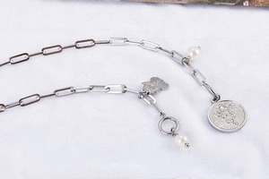 Detail of silver titanium steel necklace with rectangular links, pearls and angel pendant