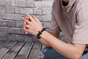 Close-up of a men's black braided leather bracelet featuring a black metal H-shaped clasp