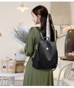 Close-up of lightweight black oxford backpack with gold zippers worn in a cafe setting